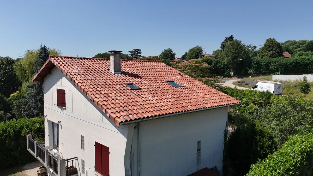 Couverture en tuiles terre cuite rénovée sur une maison aux volets rouges