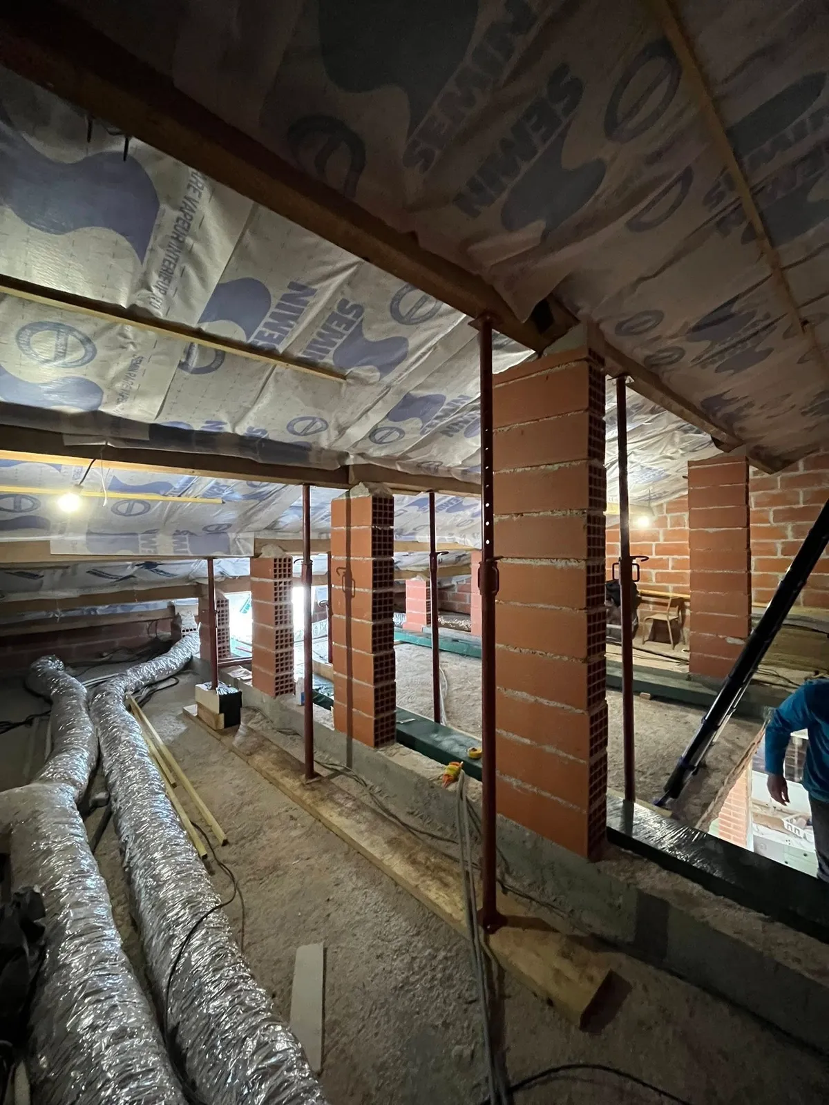 Chantier sous toiture : isolation, poutres et gaines de ventilation en cours de pose