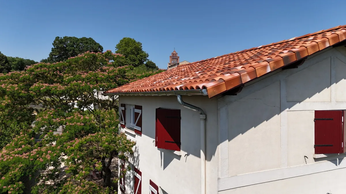 Détail de la couverture en tuiles et de la gouttière sur une maison aux volets rouges